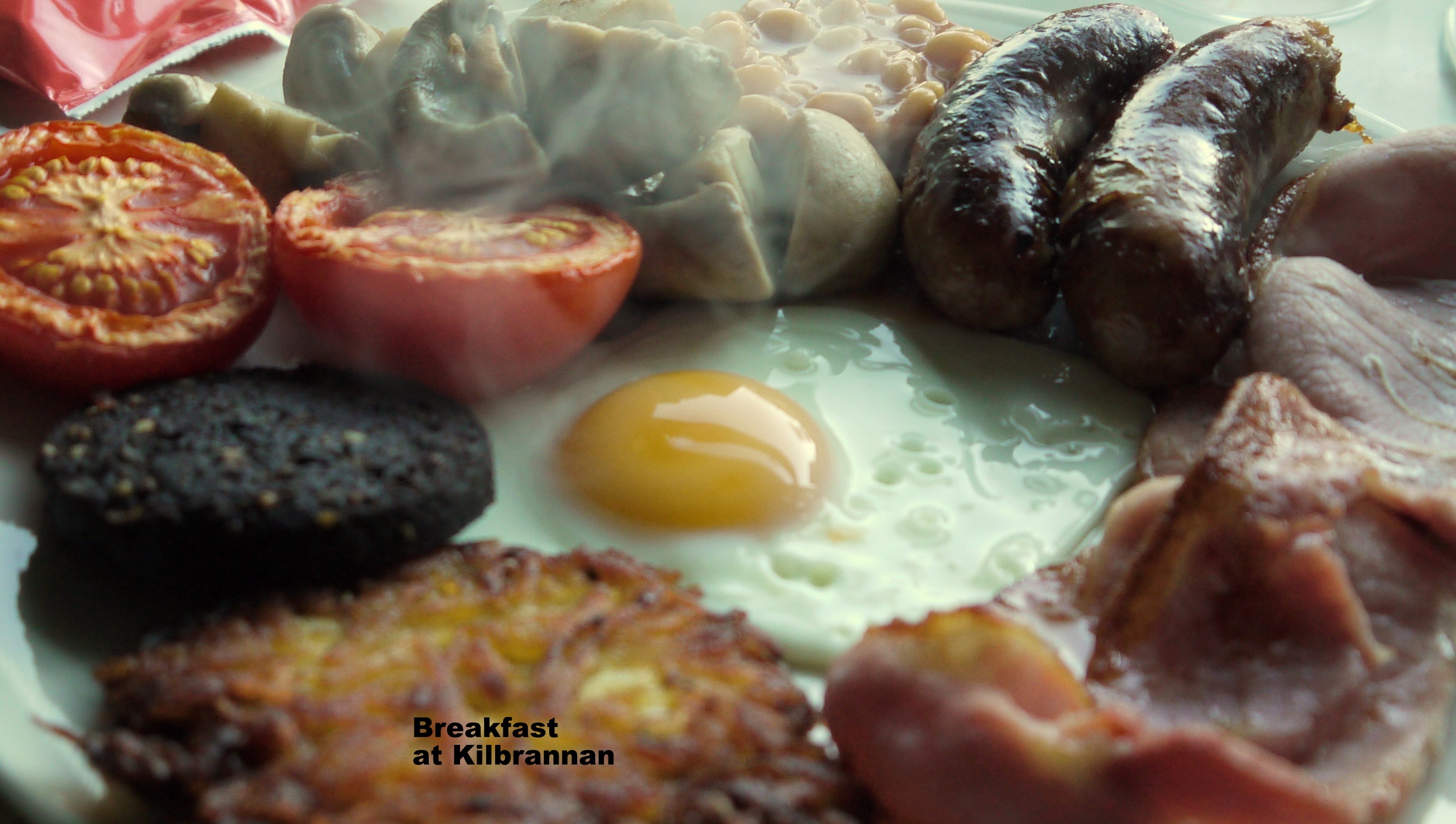 photo of a full english breakfast containing sausages, fried egg, fresh tomatoes, black pudding, hash browns, bacon and mushrooms